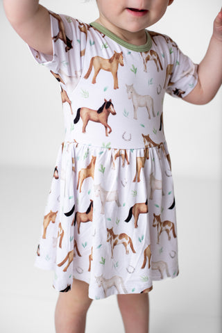 Girl wearing bamboo bodysuit dress for babies and toddlers in Perfect Ponies print